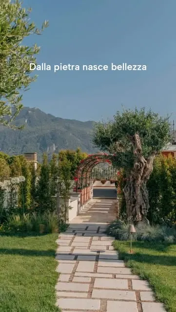 Vialetto in lastre di pietra con fuga inerbita che porta a un pergolato fiorito